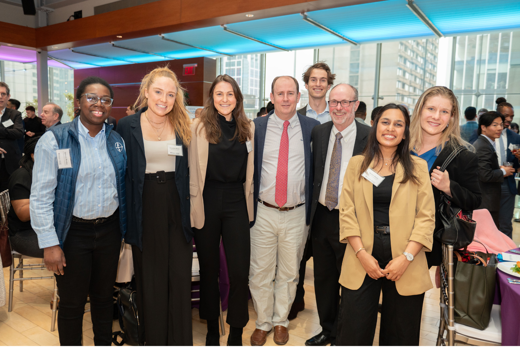 A group of people at a professional event standing together and smiling for a photo. They appear to be in a modern indoor setting with bright lighting.